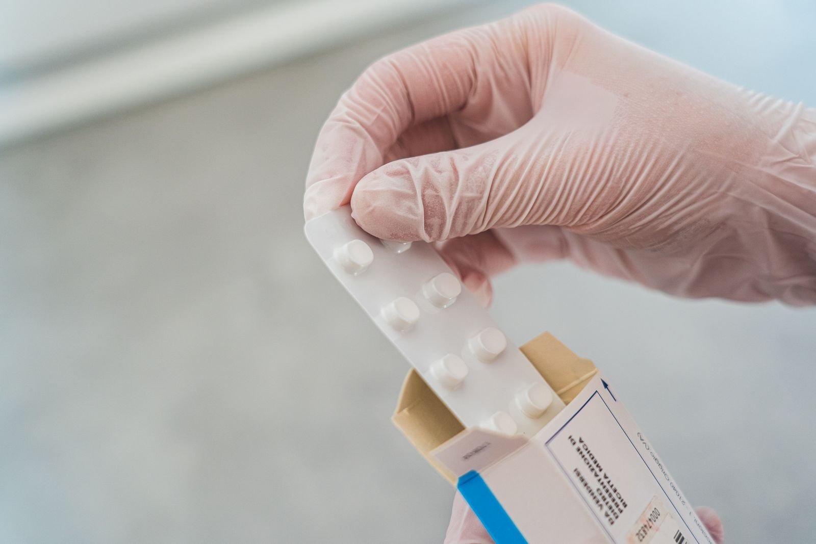 Une main tient une boîte de médicament devant un mur clair