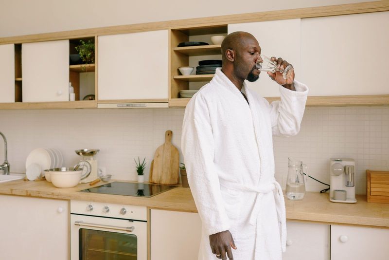 Un homme boit un verre d’eau dans sa cuisine le matin