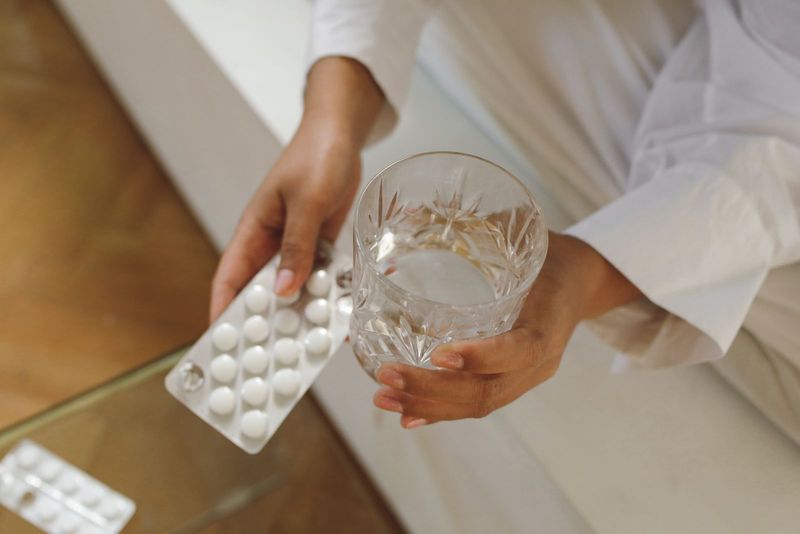 Une main tient une gélule au-dessus d’un verre d’eau