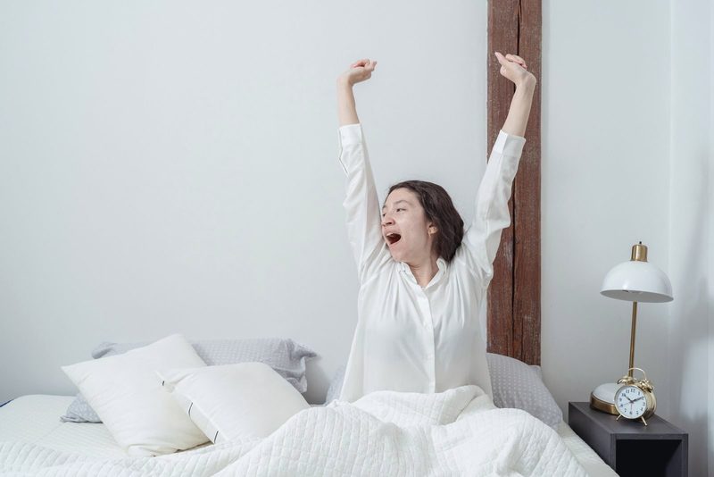 Young woman stretching on waking in a white bedroom