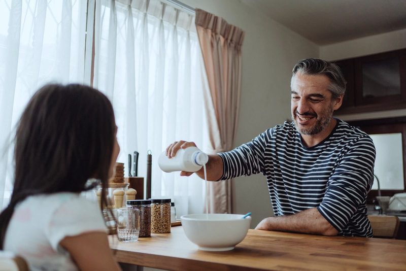 Man pouring milk into a little girl's bowl in a kitchen