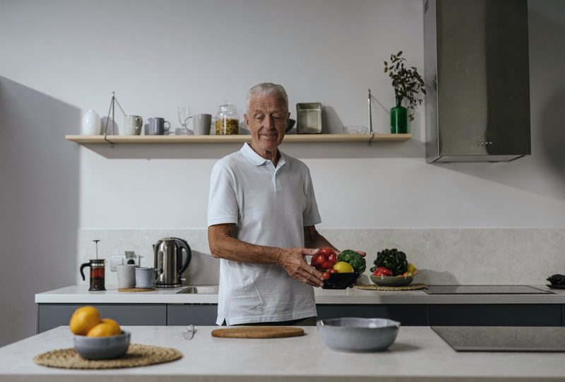 Uomo dai capelli bianchi che prepara le verdure in una cucina luminosa