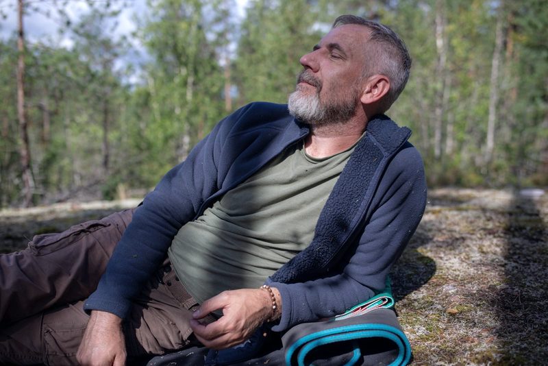 Grauhaariger Mann liegt mit geschlossenen Augen im Wald, während einer Pause beim Wandern